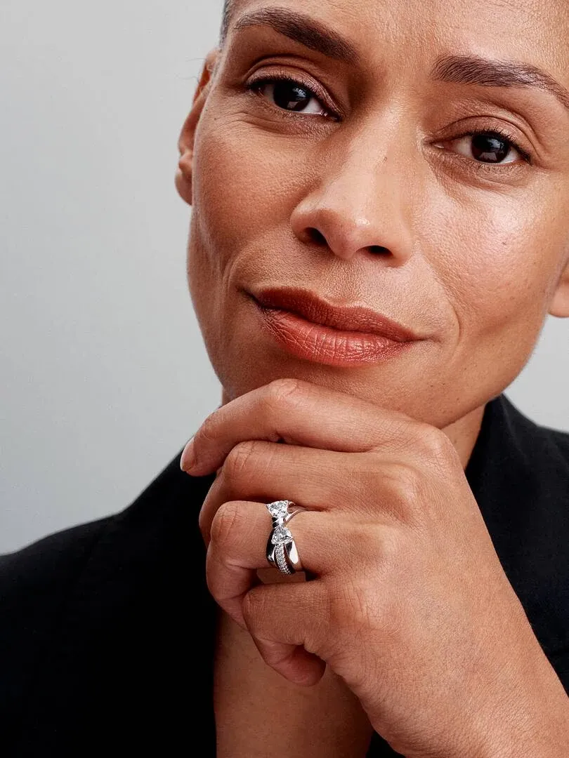 Nahaufnahme des Schleifenrings am Ringfinger, Hand unter dem Kinn auf neutralem Hintergrund abgestützt.