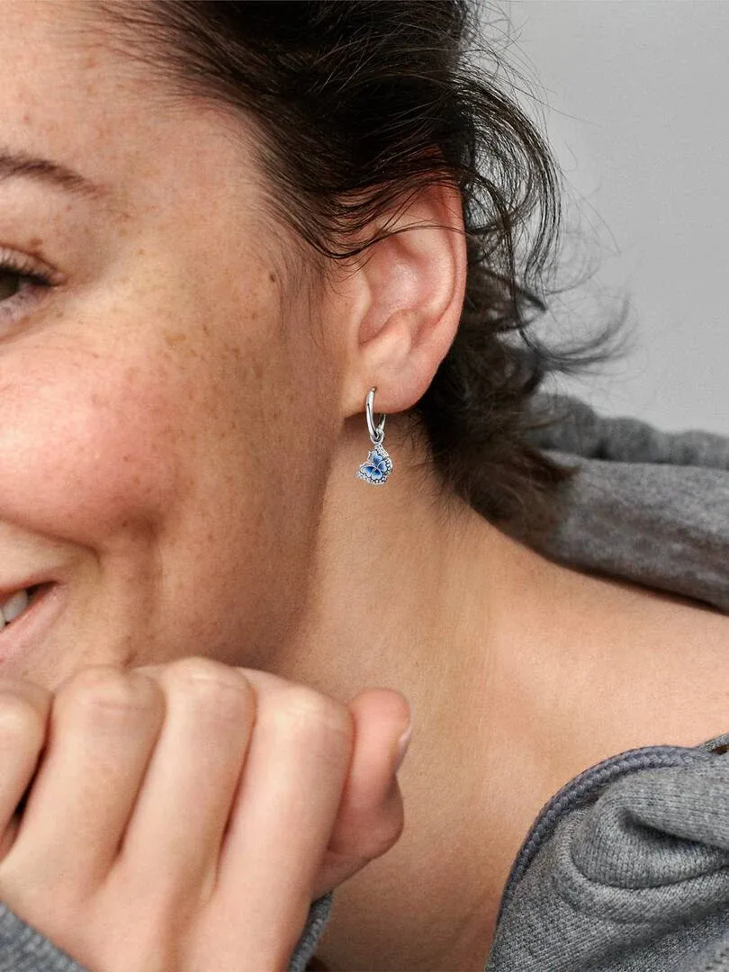 Primer plano lateral de pendiente de aro con mariposa azul puesto en la oreja, fondo desenfocado.