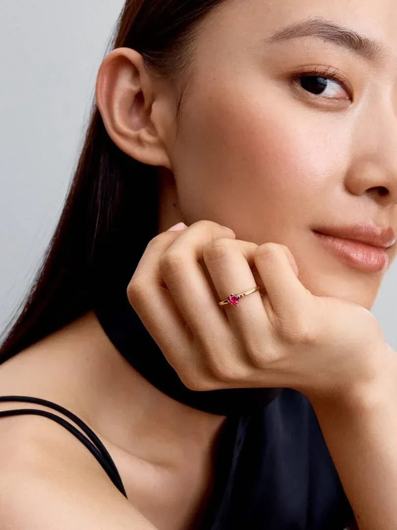 Primer plano de anillo con cristal rojo en el dedo anular, modelo apoyando la barbilla sobre la mano.