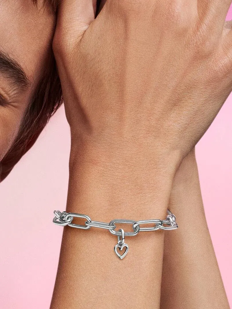 Gros plan d'un bracelet à maillons argentés avec un pendentif cœur au poignet, fond rose.