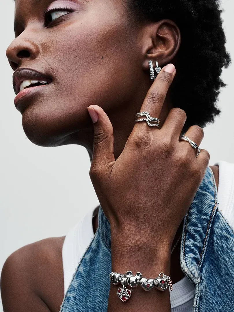 Gros plan de la main et du poignet portant un bracelet en argent et des bagues sur fond neutre clair.