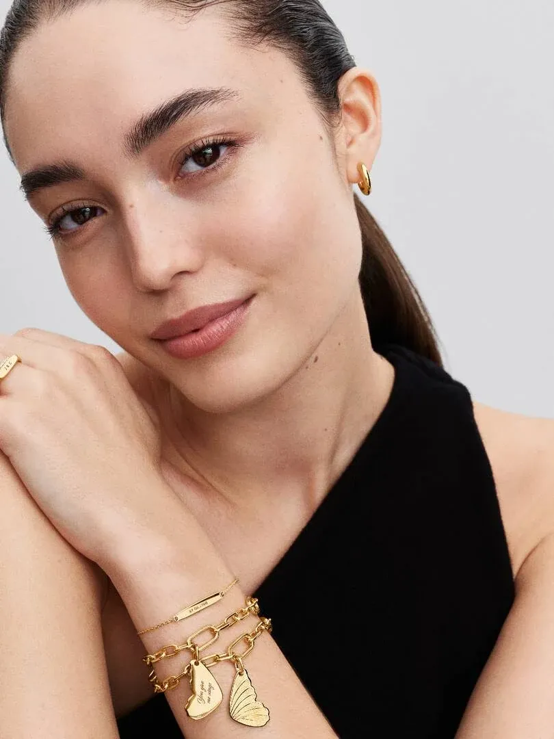 Gros plan d'un modèle portant un bracelet à charms papillon et une boucle d'oreille créole, vue de profil.