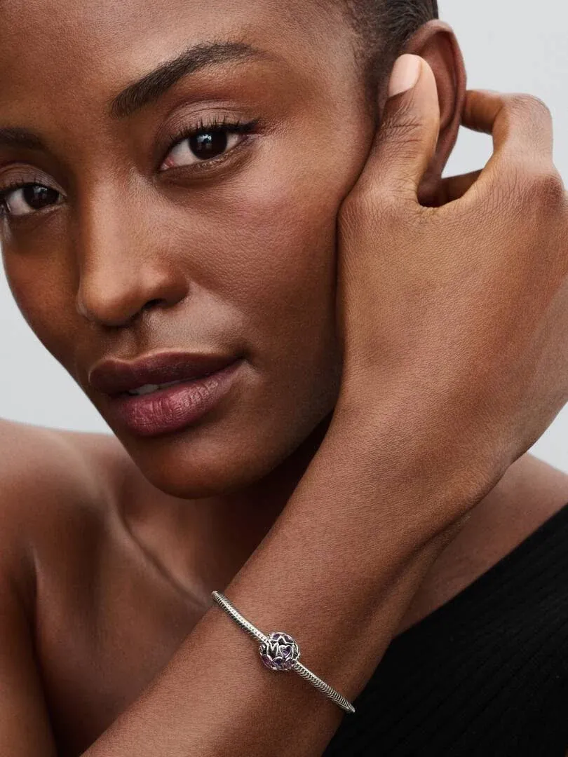 Nahaufnahme des Handgelenks mit dem lavendelfarbenen Herz-Charm, Seitenansicht vor neutralem Hintergrund.