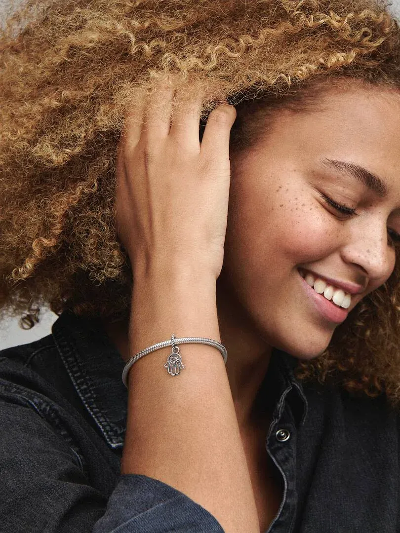 Primer plano de la muñeca con el charm de mano de Fátima en una pulsera, modelo sonriente de perfil.