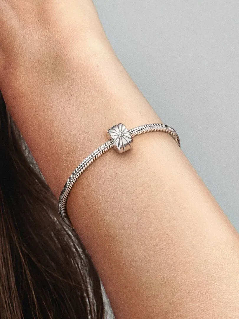 Primer plano del charm de clip en la muñeca, toma lateral con fondo neutro desenfocado.