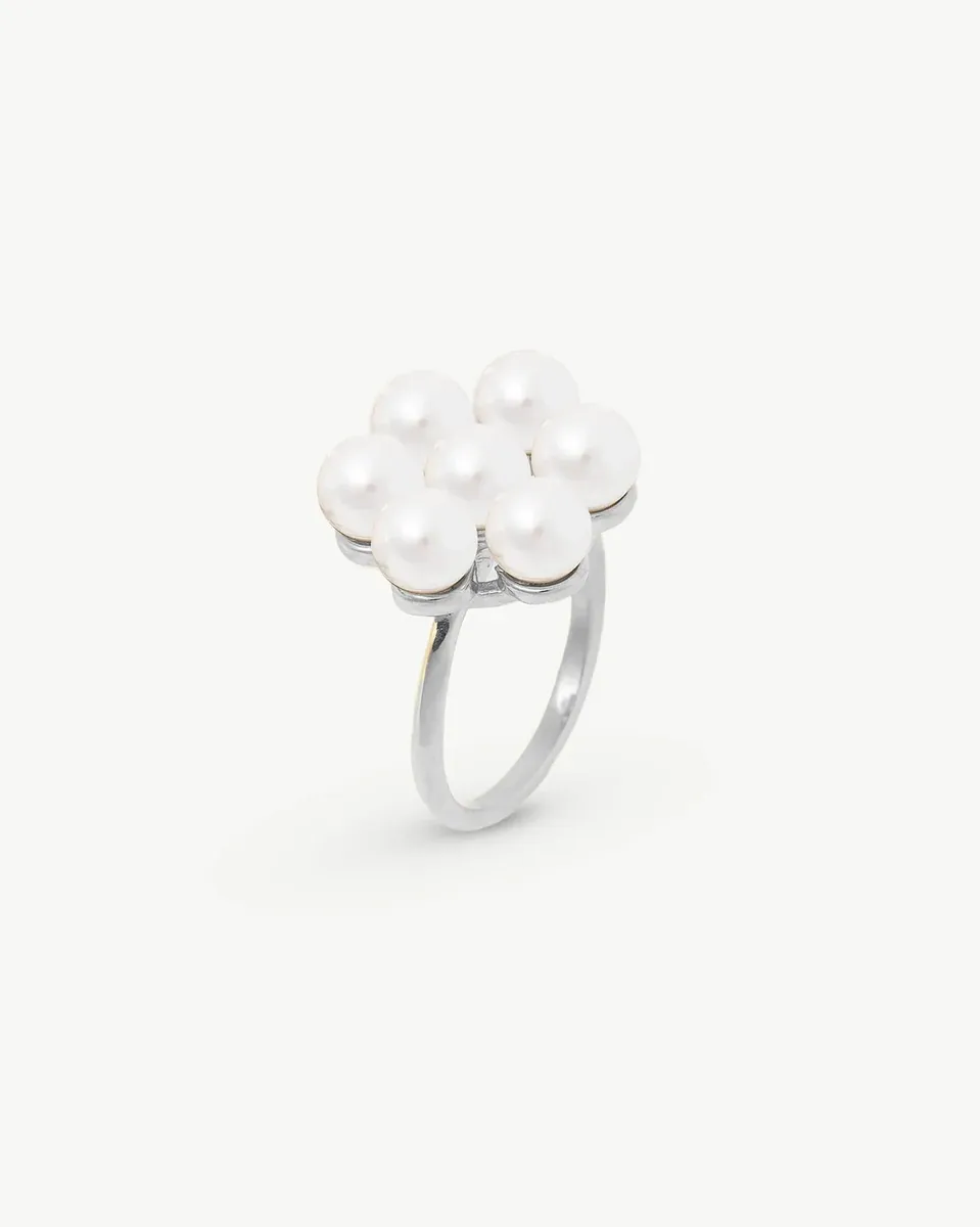 Anillo de perlas en forma de flor visto desde un ángulo lateral, sobre fondo blanco.