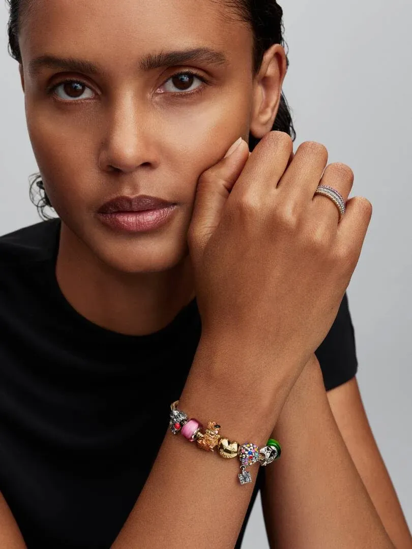 Gros plan d'une main portant un bracelet à charms et une bague sur fond neutre.