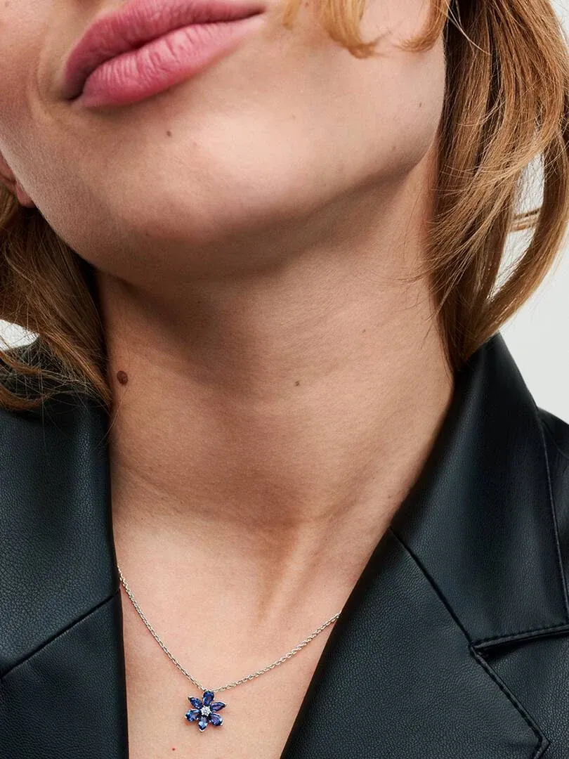 Gros plan du pendentif floral bleu sur le cou d'un mannequin, vue de face avec veste sombre.