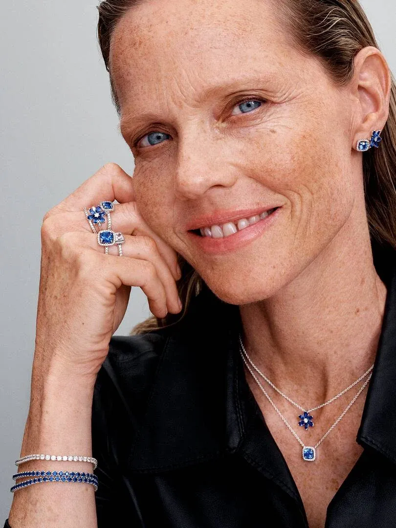 Model wearing blue jewelry set including ring, earrings, necklace, and bracelet against neutral background.