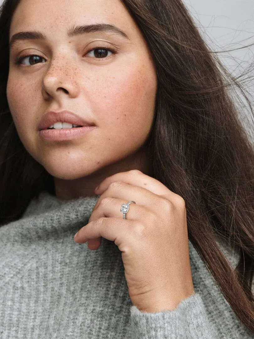 Close-up van de ring met vierkante steen aan de vinger van een model, neutrale achtergrond en grijze trui.