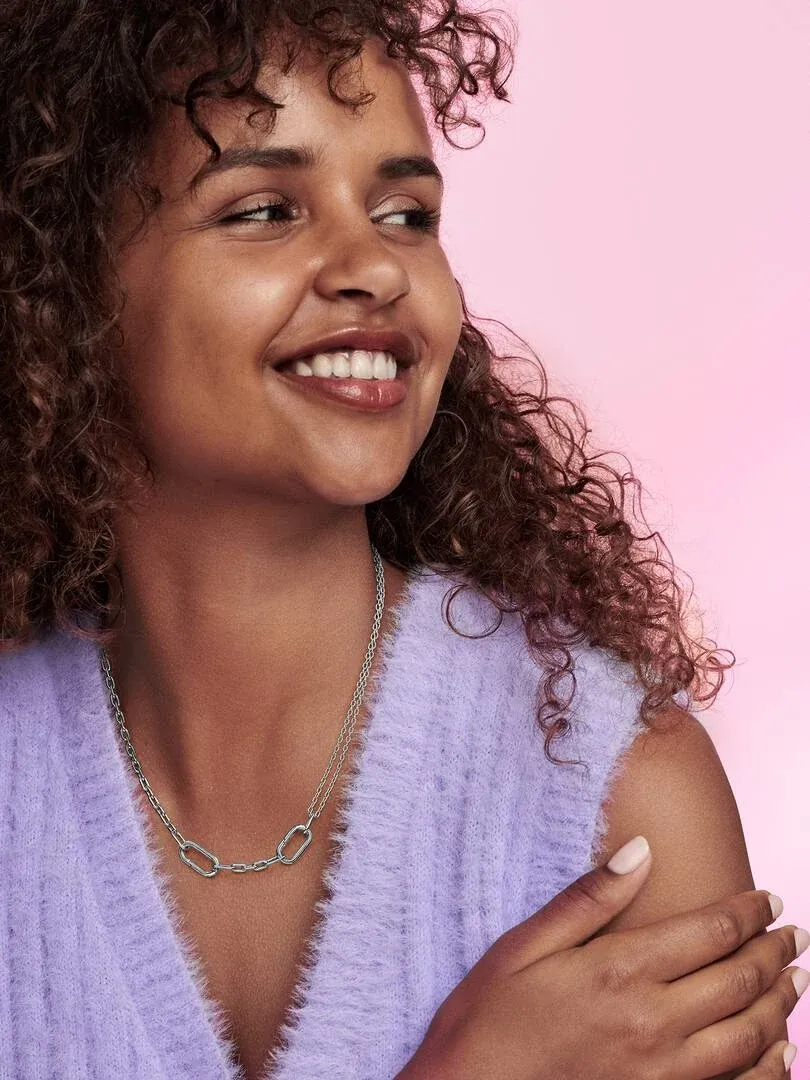 Primer plano del collar de eslabones sobre el cuello de una modelo, fondo rosa suave.