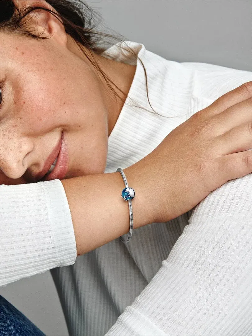 Primer plano del clip de globo terráqueo azul en una pulsera, puesto en la muñeca de una modelo.