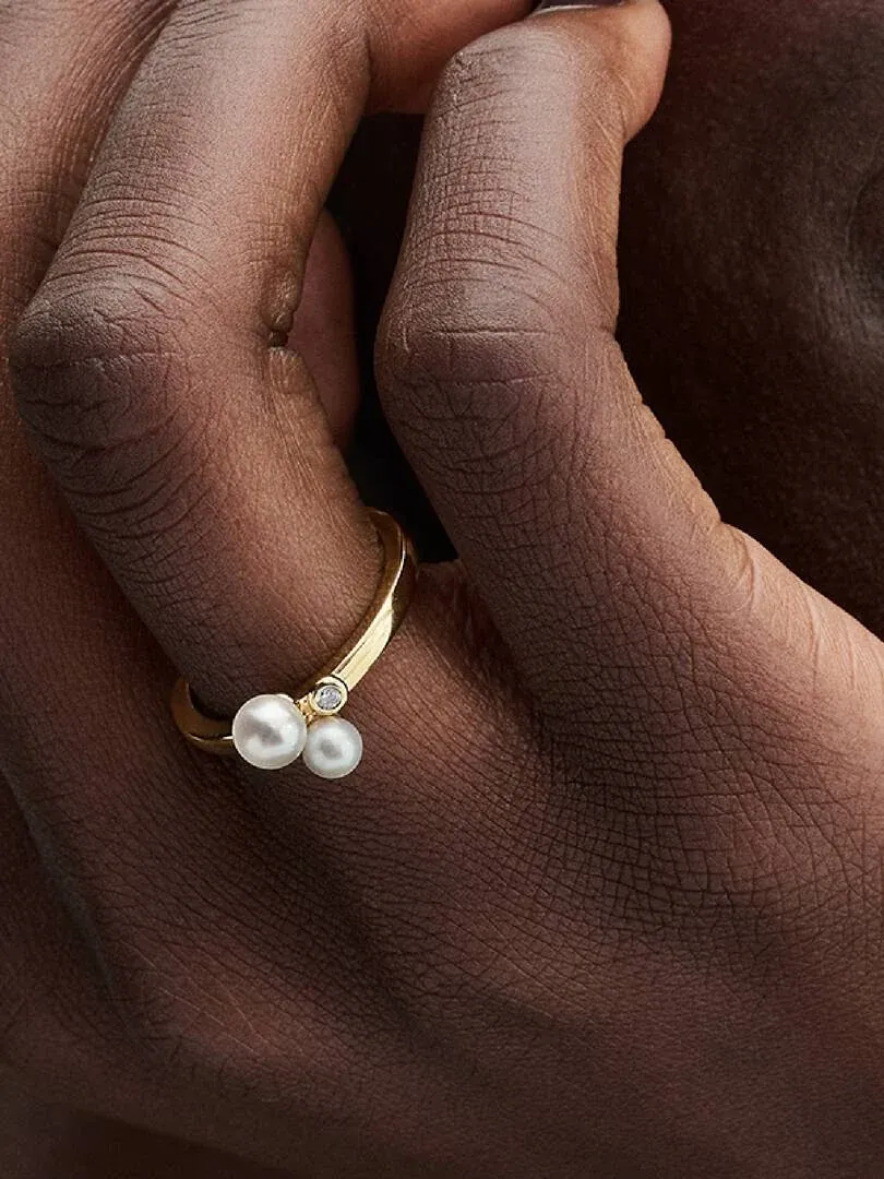 Primer plano lateral del anillo con perlas y circonita puesto en un dedo, sobre piel oscura.