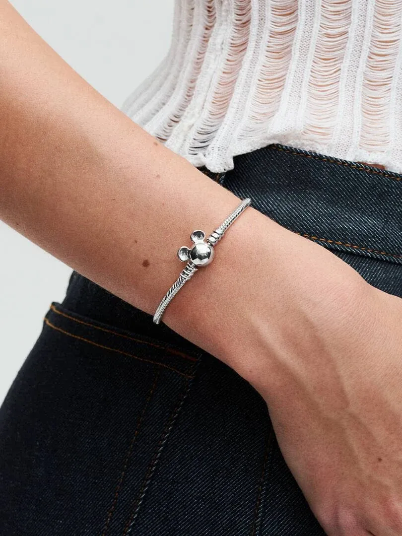 Gros plan du bracelet avec fermoir Mickey Mouse sur un poignet, fond jean et haut blanc.