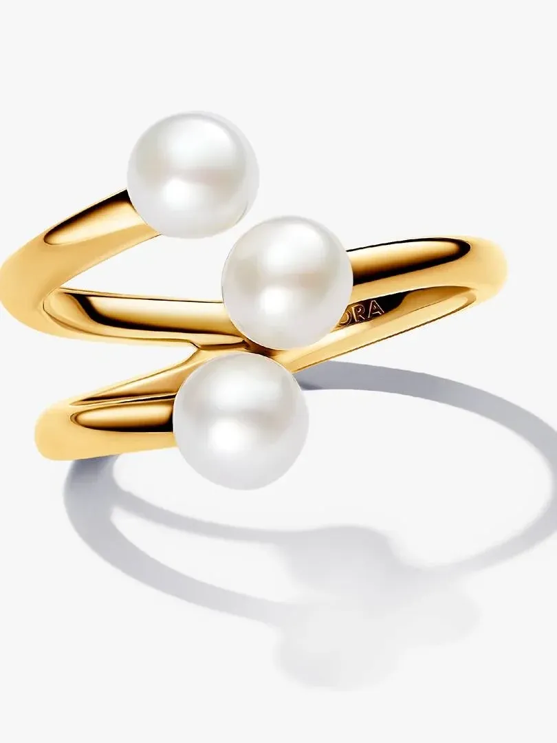 Anillo de tres bandas con perlas blancas, vista lateral en ángulo sobre fondo blanco con sombra suave.