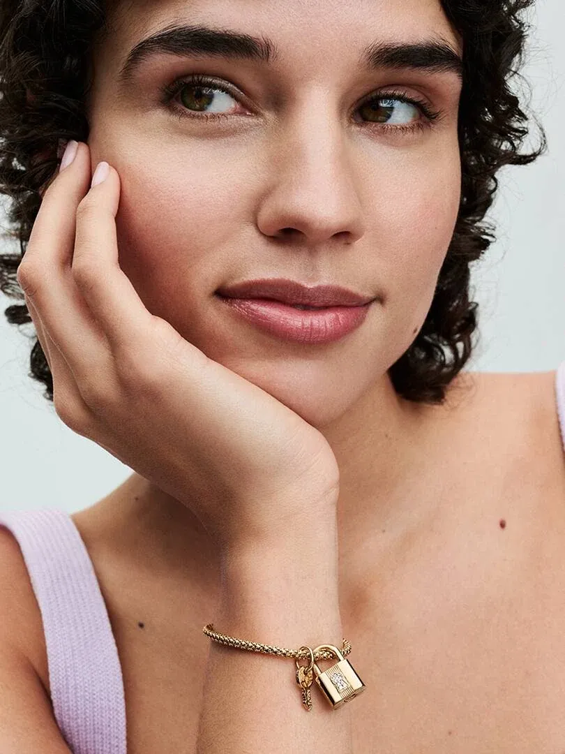 Close-up of padlock and key charm bracelet on a model's wrist, soft focus background.