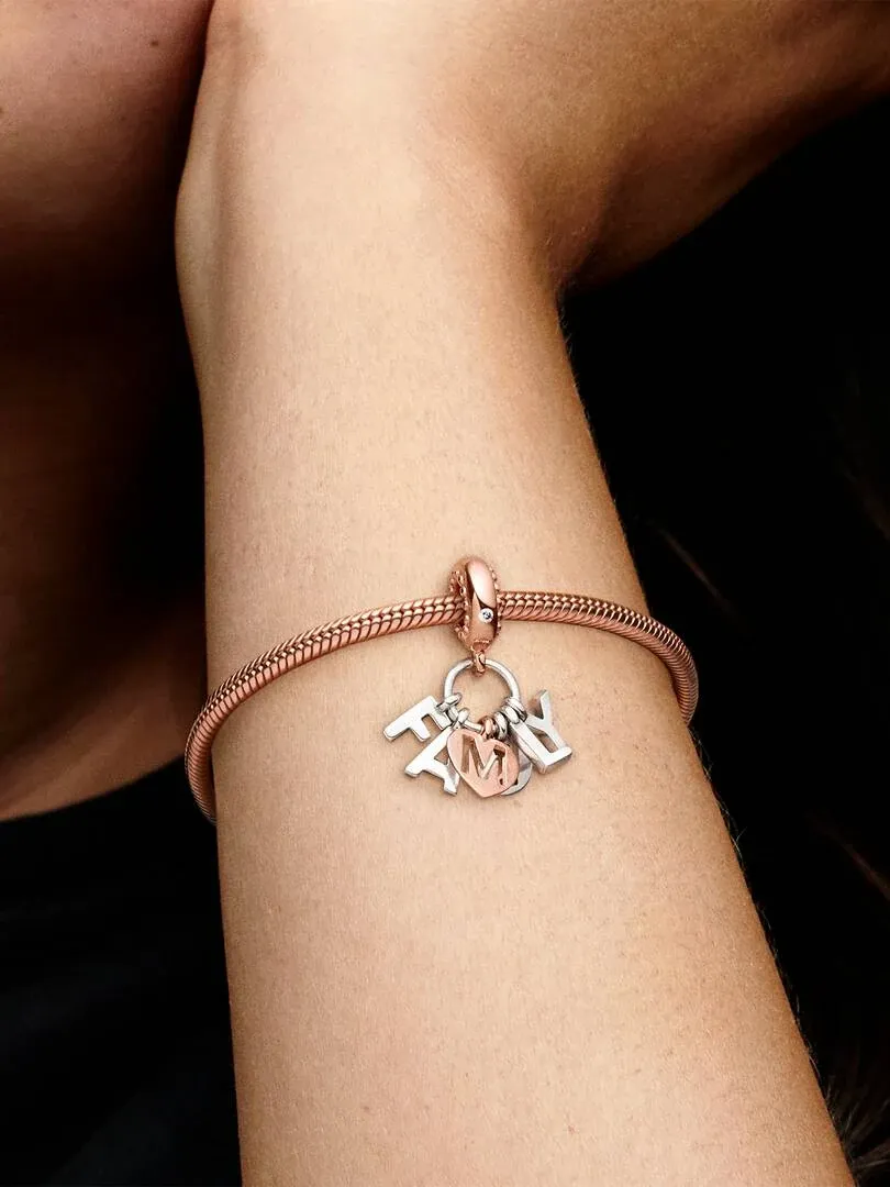 Primer plano del charm de letras en un brazalete de oro rosa sobre la muñeca, toma lateral con fondo oscuro.