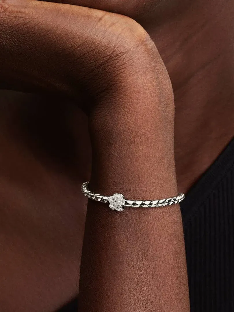 Primer plano de un charm de huella en una pulsera de plata, puesto en la muñeca de una modelo.