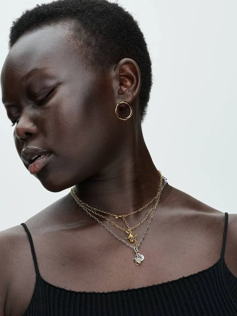 Gros plan de colliers superposés avec charms sur le cou d'un modèle, vue de profil sur fond blanc.