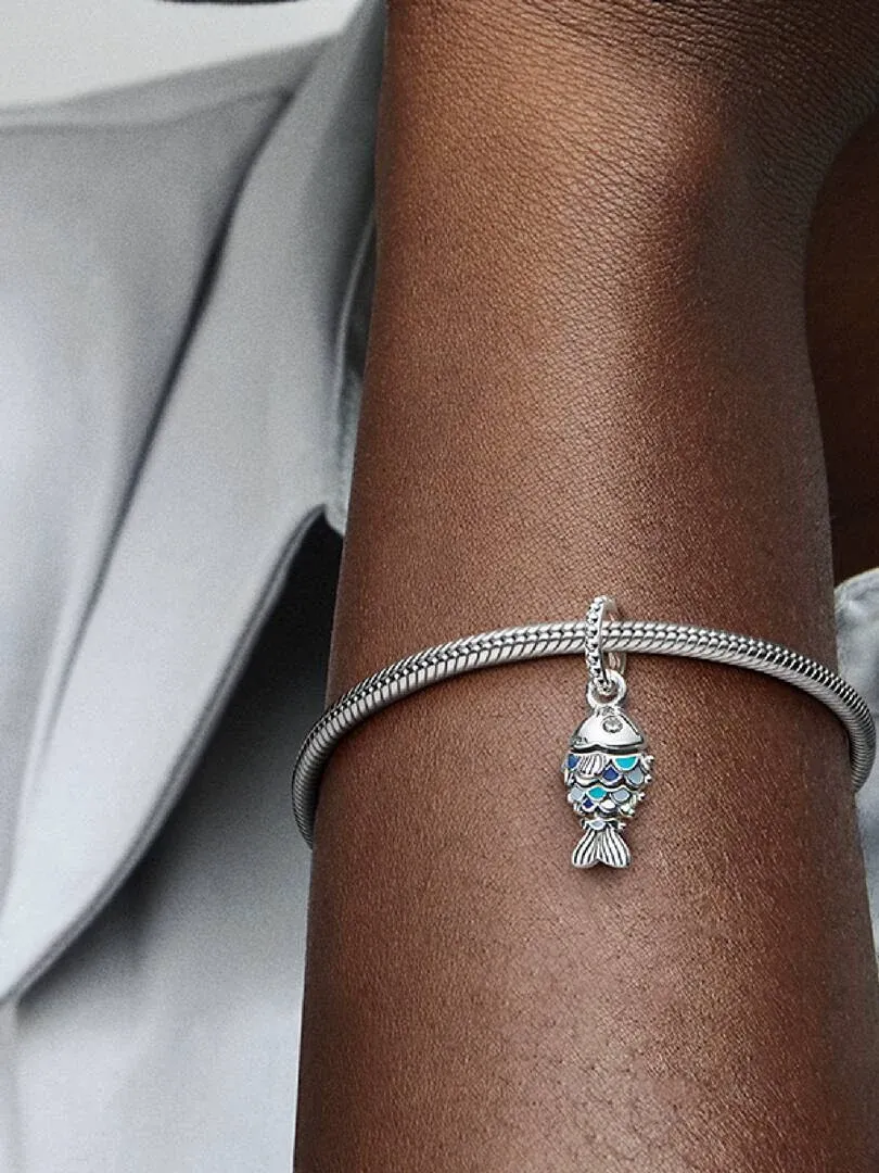 Primer plano del charm de pez azul colgando de una pulsera de plata en la muñeca, fondo desenfocado.