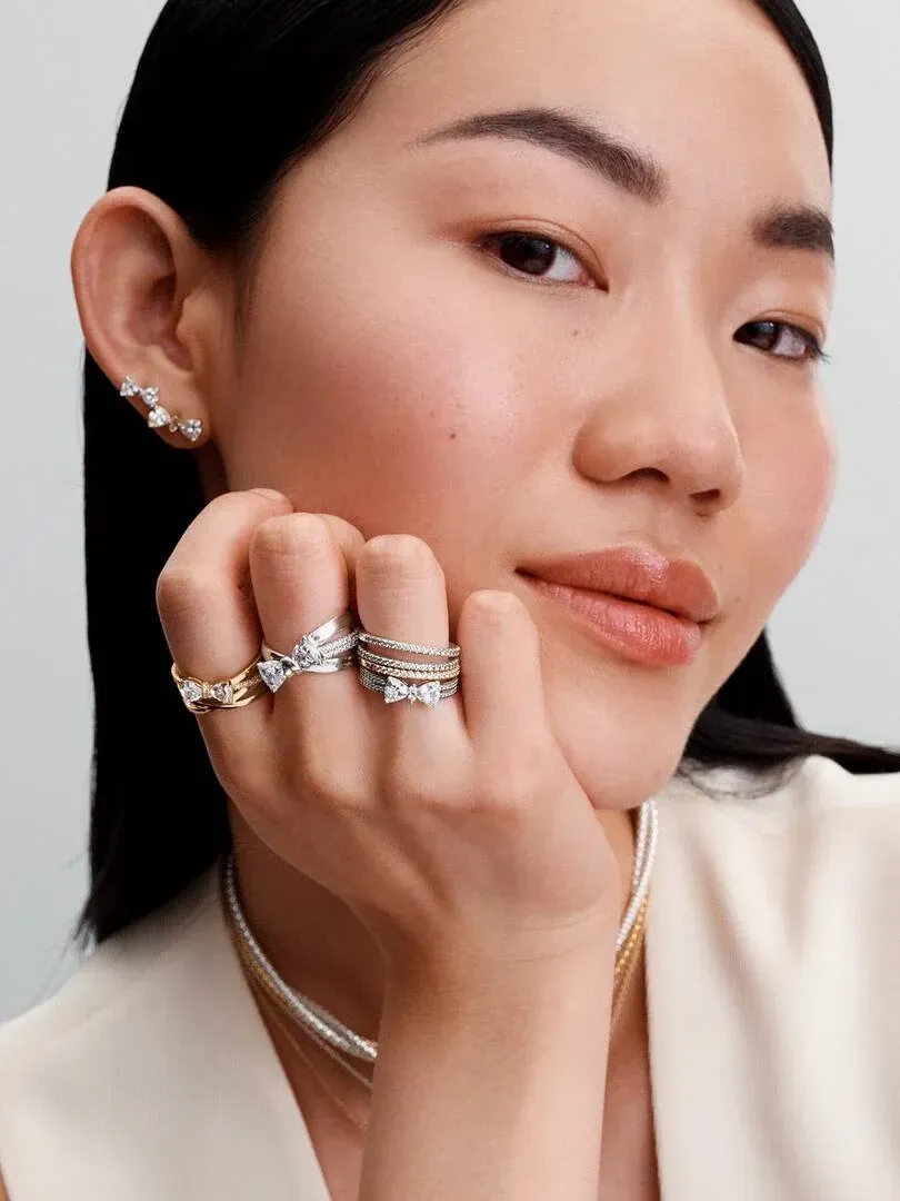 Nahaufnahme einer Hand mit mehreren gekreuzten Ringbanden und Ohrringen, Model vor neutralem Hintergrund.