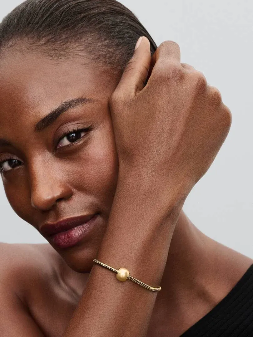 Primer plano de pulsera con charm dorado en la muñeca, toma lateral sobre modelo con fondo neutro.