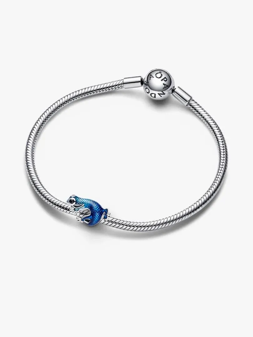 Charm de geco azul sobre pulsera de plata, vista superior en ángulo, fondo blanco neutro.