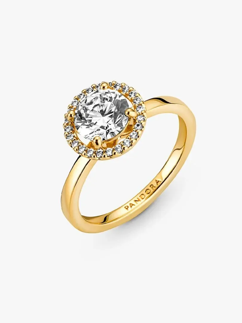 Anillo de oro con gema central y halo, vista lateral en ángulo sobre fondo blanco.