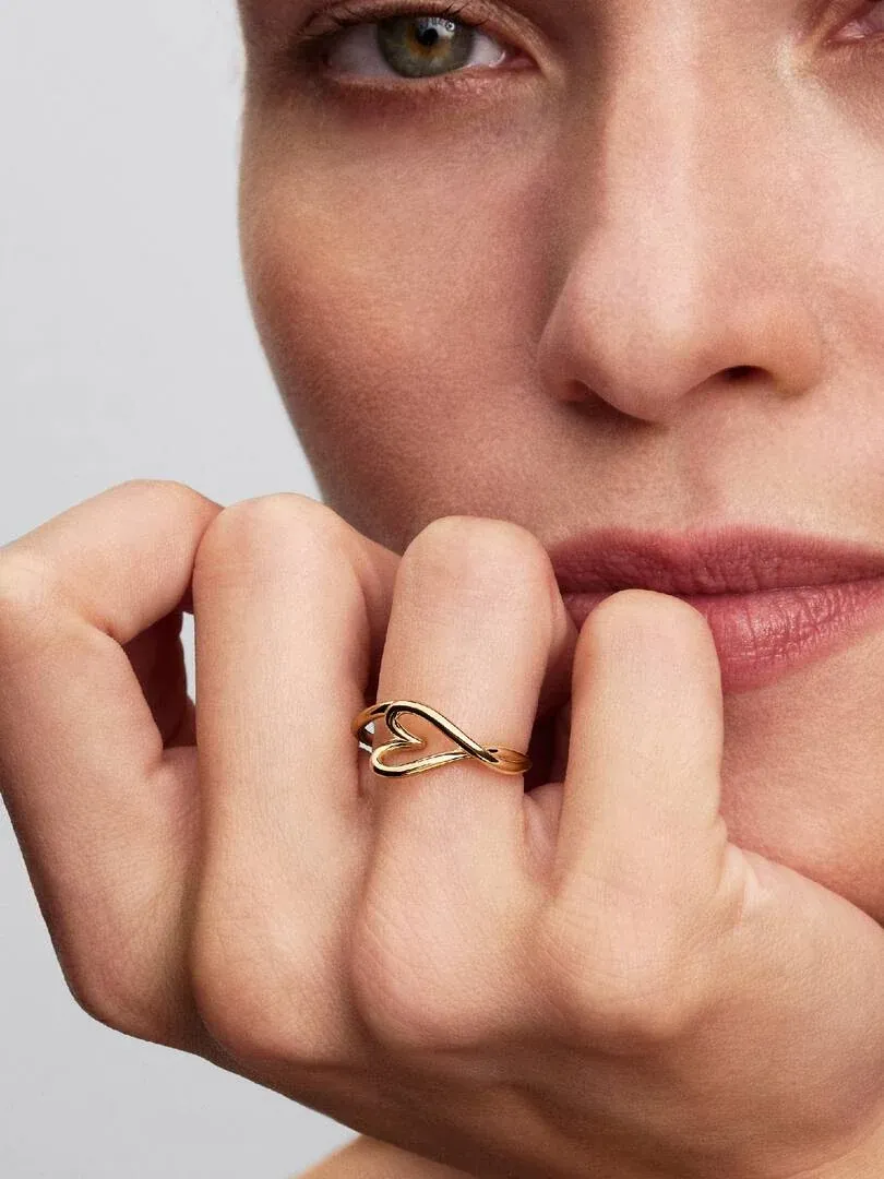 Primer plano del anillo de corazón dorado puesto en el dedo, mano cerca del rostro, fondo desenfocado.