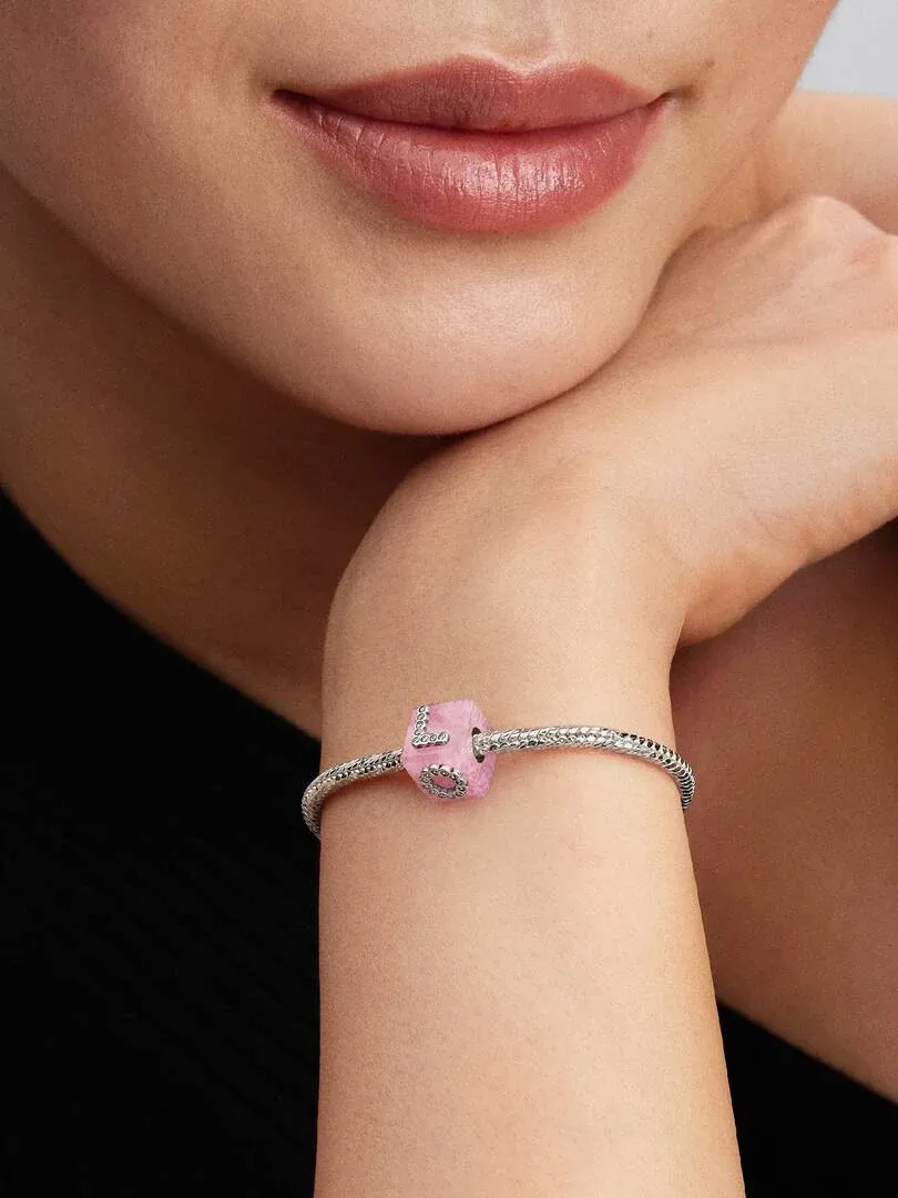 Close-up van een roze kristallen charm aan een armband, gedragen om de pols van een model tegen een donkere achtergrond.