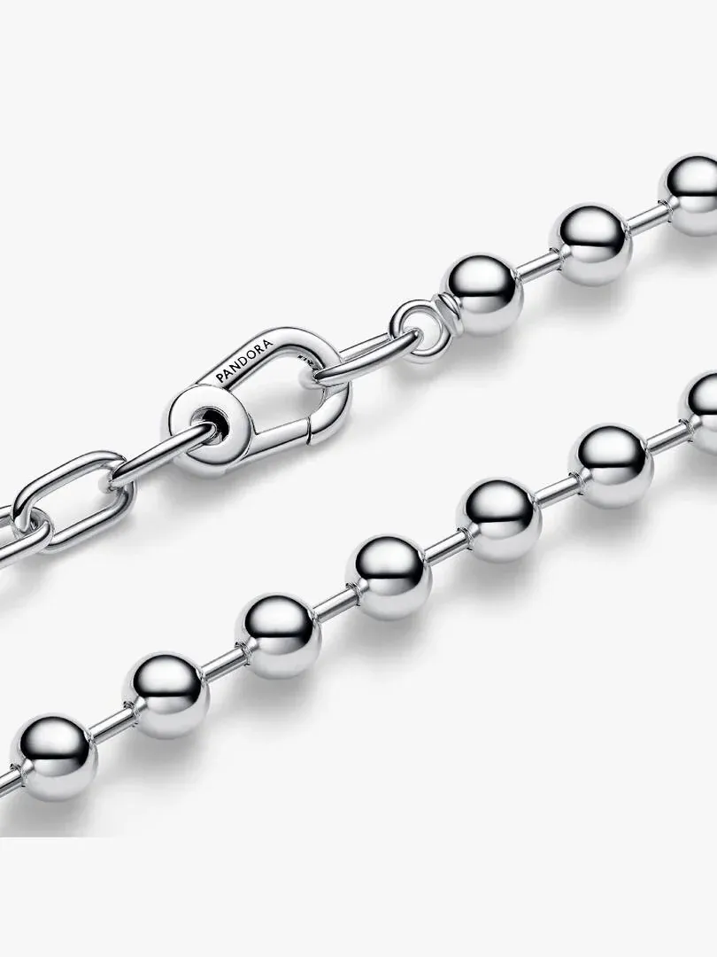 Primer plano diagonal de eslabones y cuentas de plata sobre fondo blanco, enfoque en el cierre grabado.