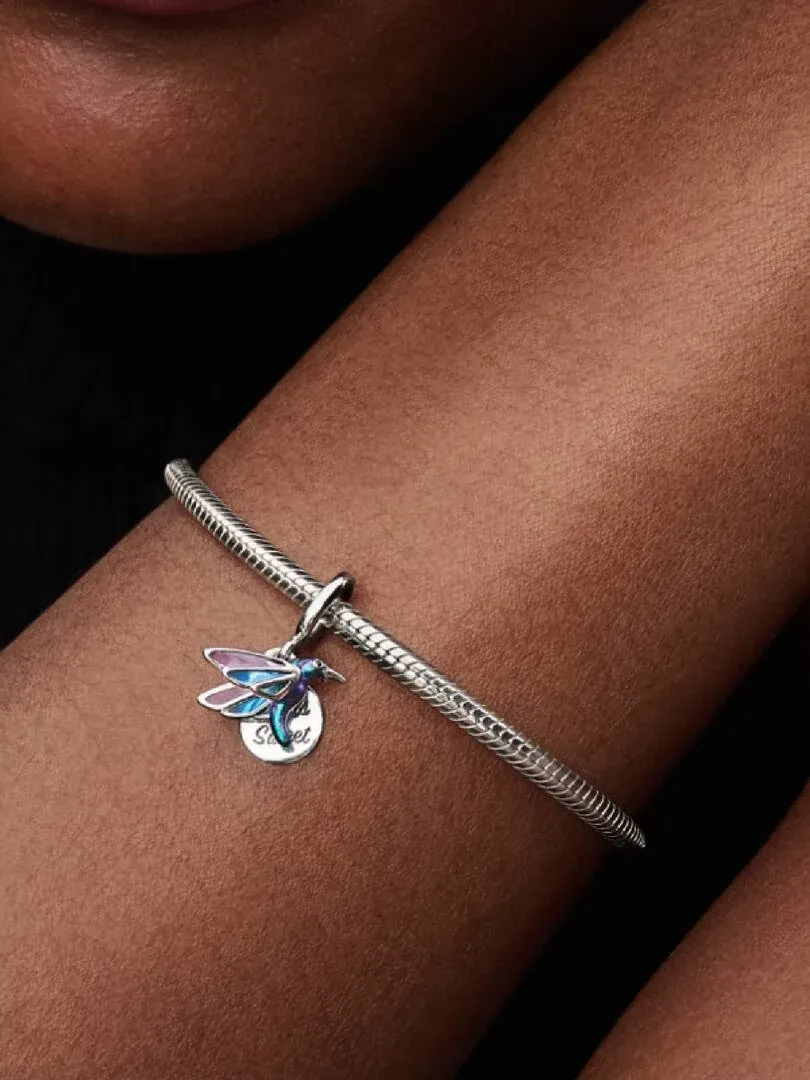 Charm de colibrí con esmalte iridiscente en una pulsera de plata, toma lateral sobre la muñeca.