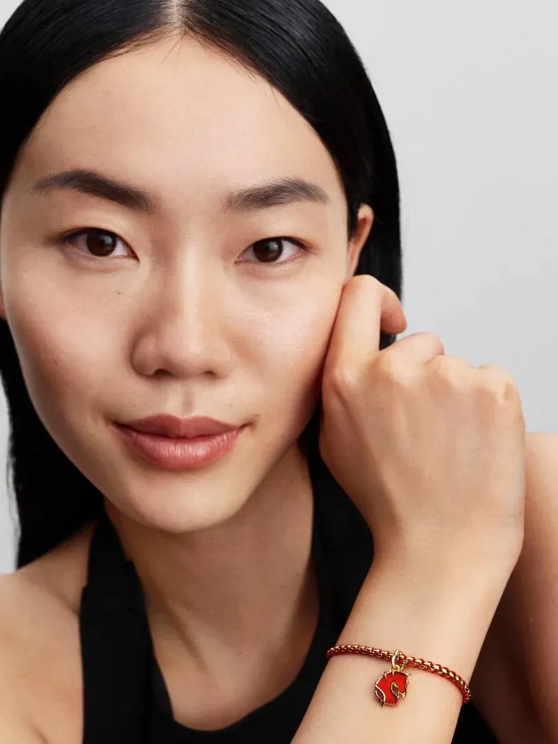 Close-up van een pols met een armband en rood paard charm, model tegen neutrale achtergrond.