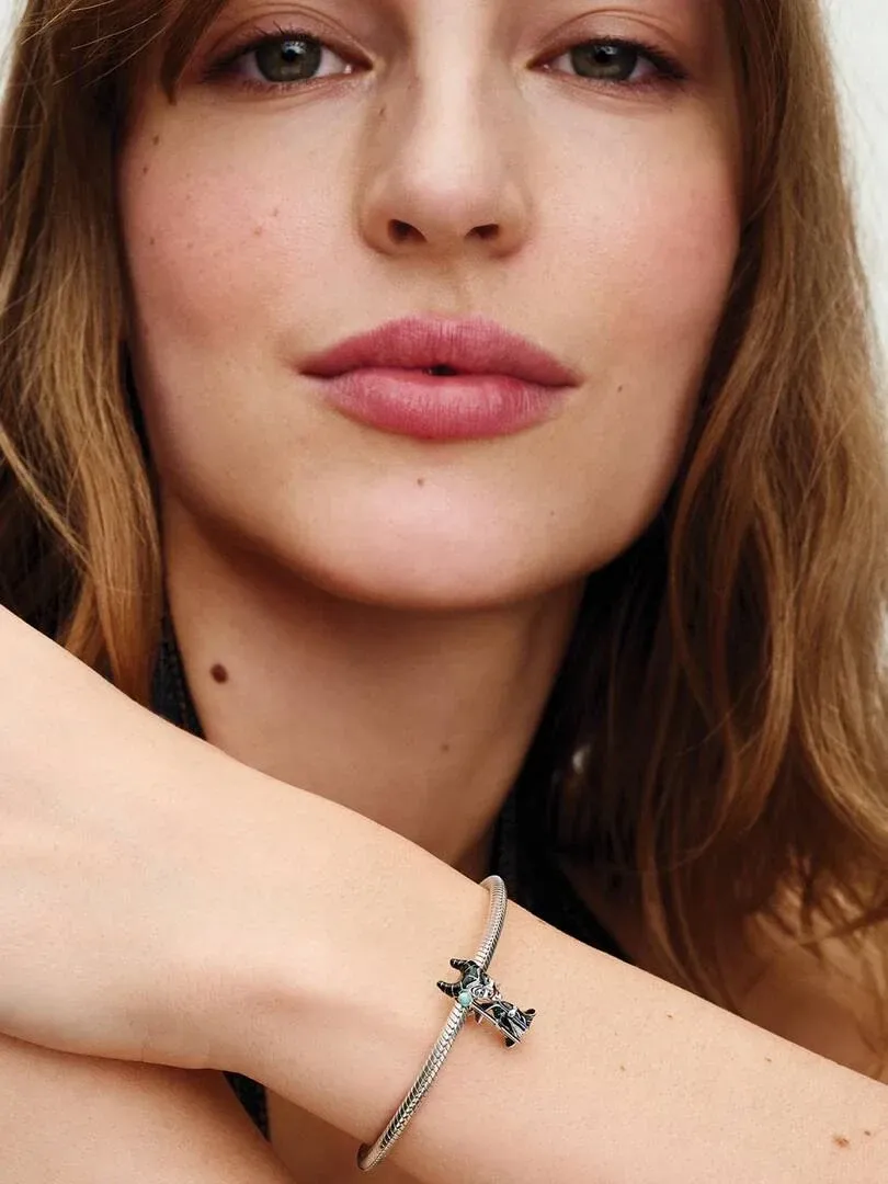 Primer plano de un charm en una pulsera de plata, sujeto en la muñeca de una modelo con fondo desenfocado.