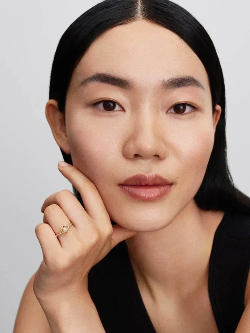 Primer plano de mano femenina apoyada en la barbilla, mostrando el anillo con perla en el dedo anular.