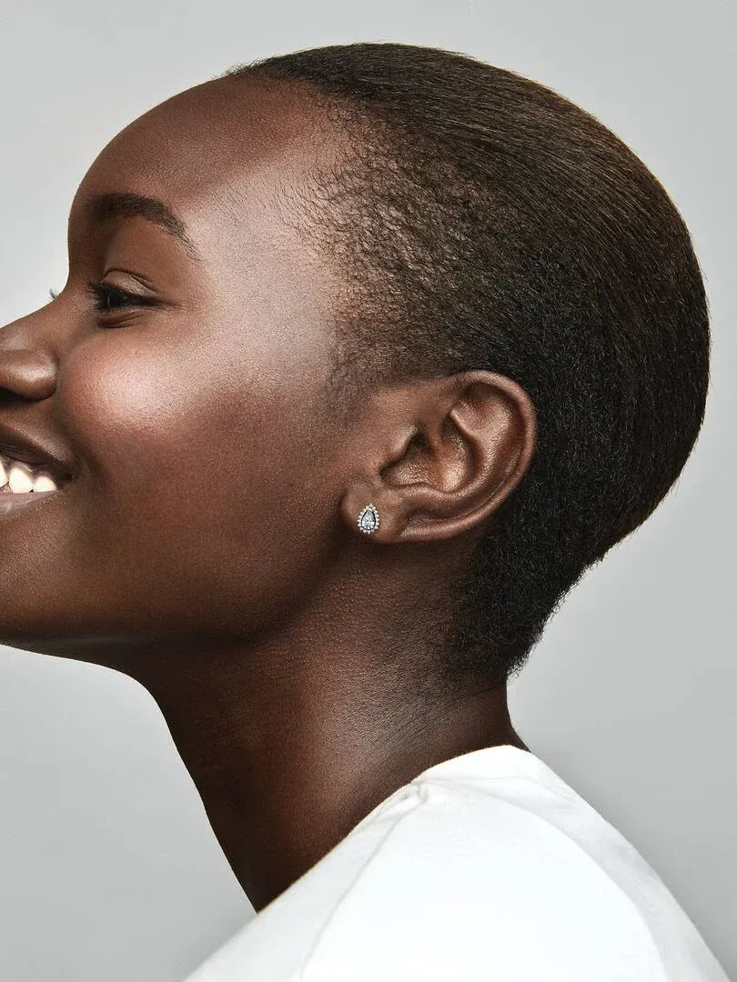Primer plano lateral de pendiente de botón con gema en forma de pera puesto en la oreja, fondo gris neutro.