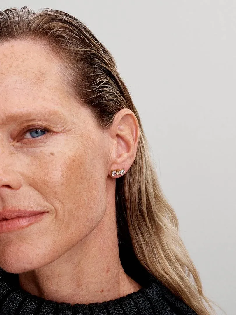 Primer plano lateral de pendiente de lazo con circonitas en el lóbulo de una modelo, fondo neutro claro.