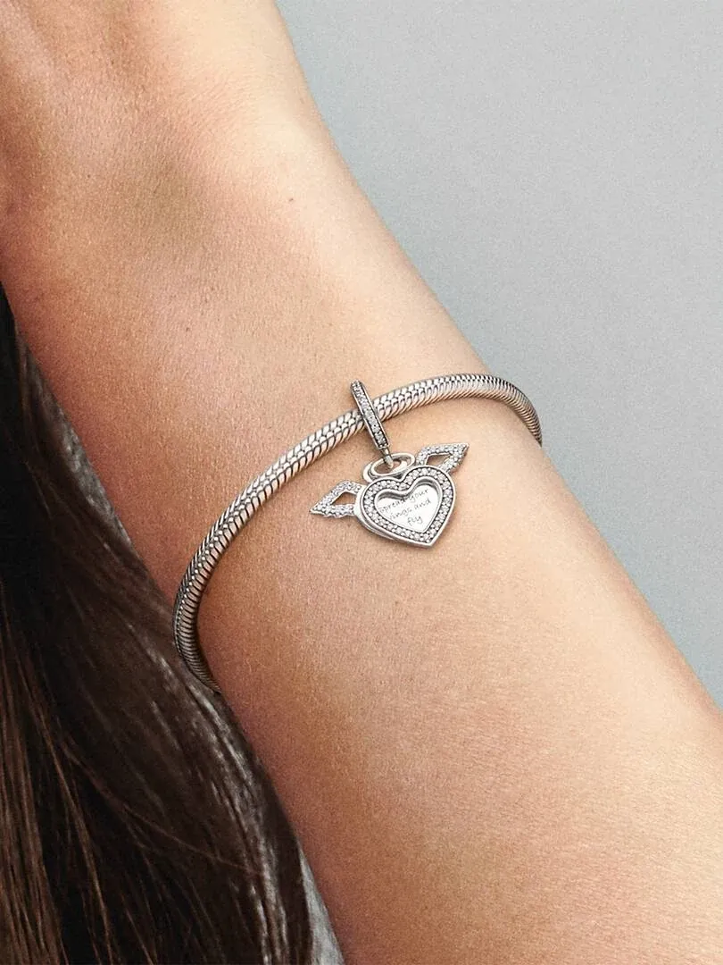 Primer plano del charm de corazón y alas en una pulsera de plata, sobre la muñeca con fondo neutro.