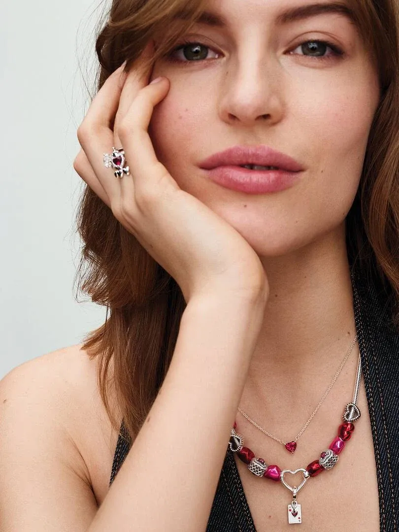 Gros plan d'un modèle portant un collier de perles rouges et une bague en argent, vue de face sur fond neutre.