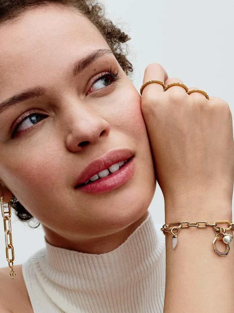 Primer plano de modelo con anillo dorado y pulsera de eslabones, toma lateral sobre fondo blanco.