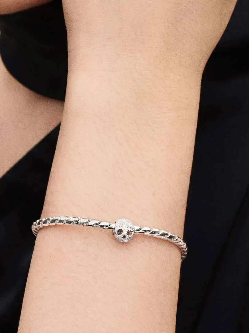 Primer plano de la pulsera con charm de calavera en una muñeca, toma lateral sobre fondo oscuro.