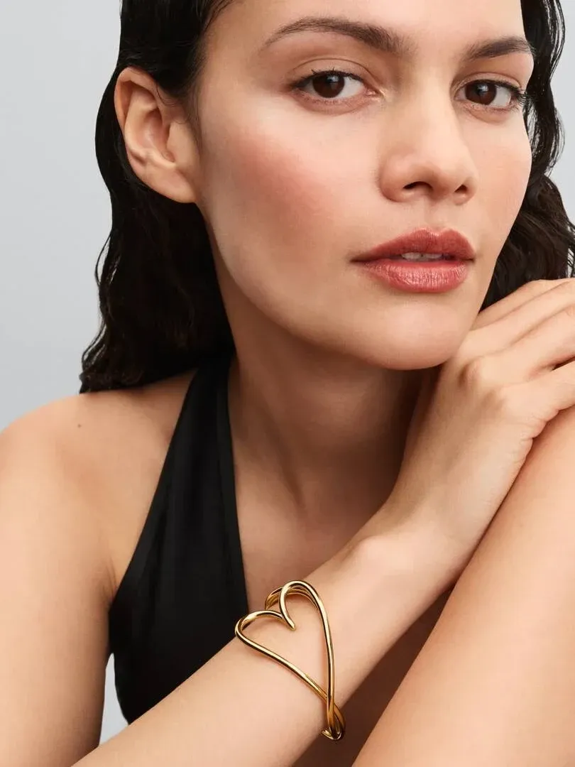 Primer plano de la pulsera rígida dorada con forma de corazón puesta en la muñeca, toma lateral sobre modelo.