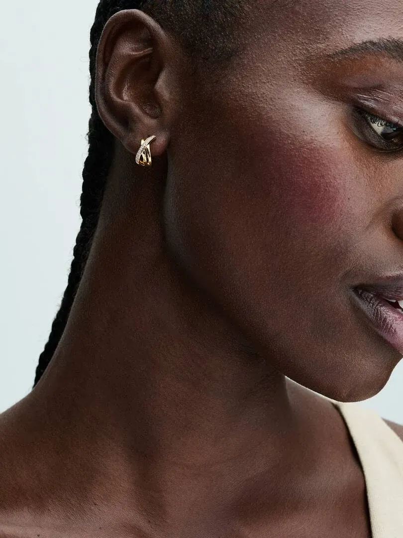 Side close-up of a gold hoop earring with pavé stones on a model's ear, neutral background.
