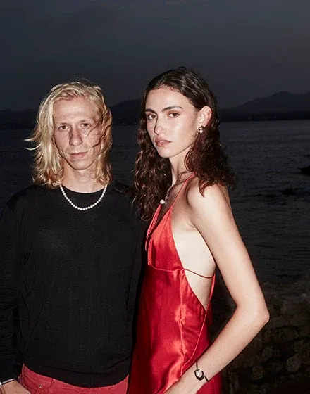 Couple face à la mer au crépuscule ; elle porte le bracelet en perles au poignet et un collier de perles.