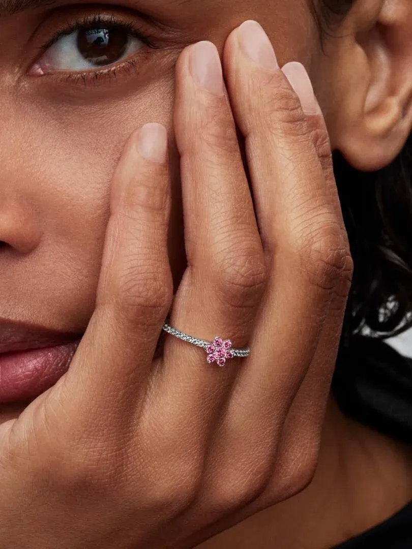 Close-up of the pink flower ring worn on a finger, hand resting near the face.