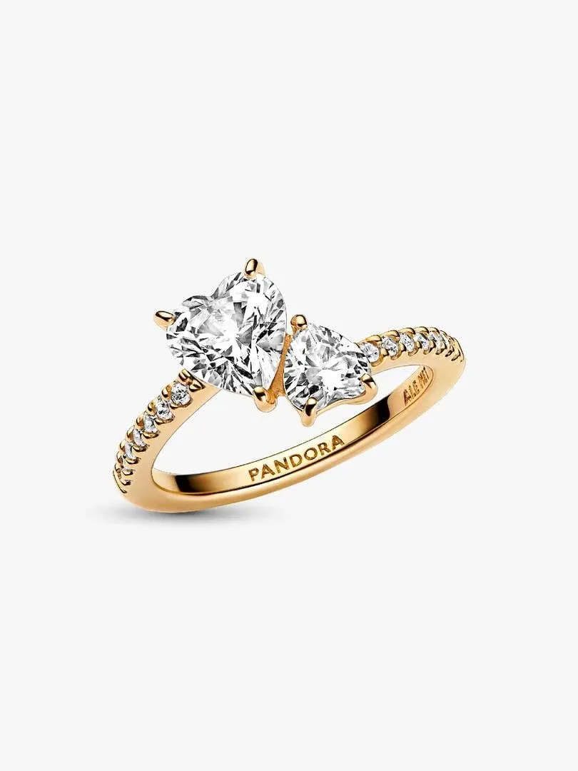Anillo de doble corazón visto en ángulo lateral, fondo blanco, detalle del pavé y grabado de marca.
