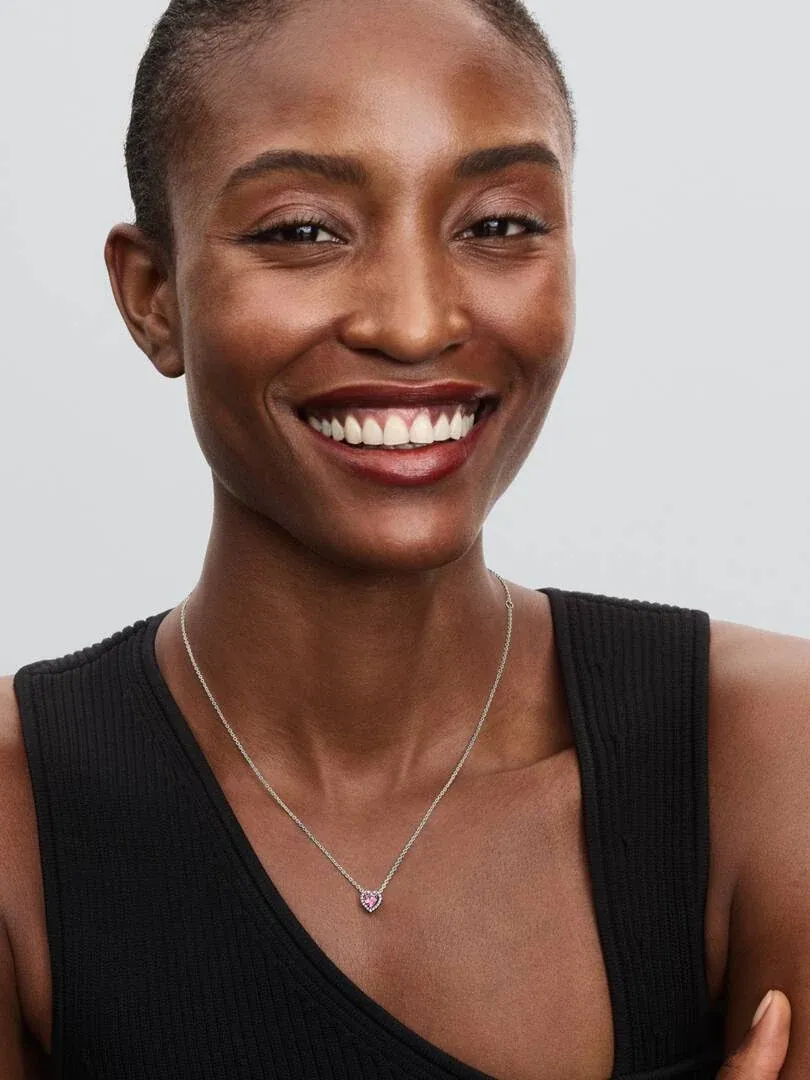 Gros plan d'un collier avec pendentif cœur rose porté sur le cou d'un modèle, fond neutre clair.