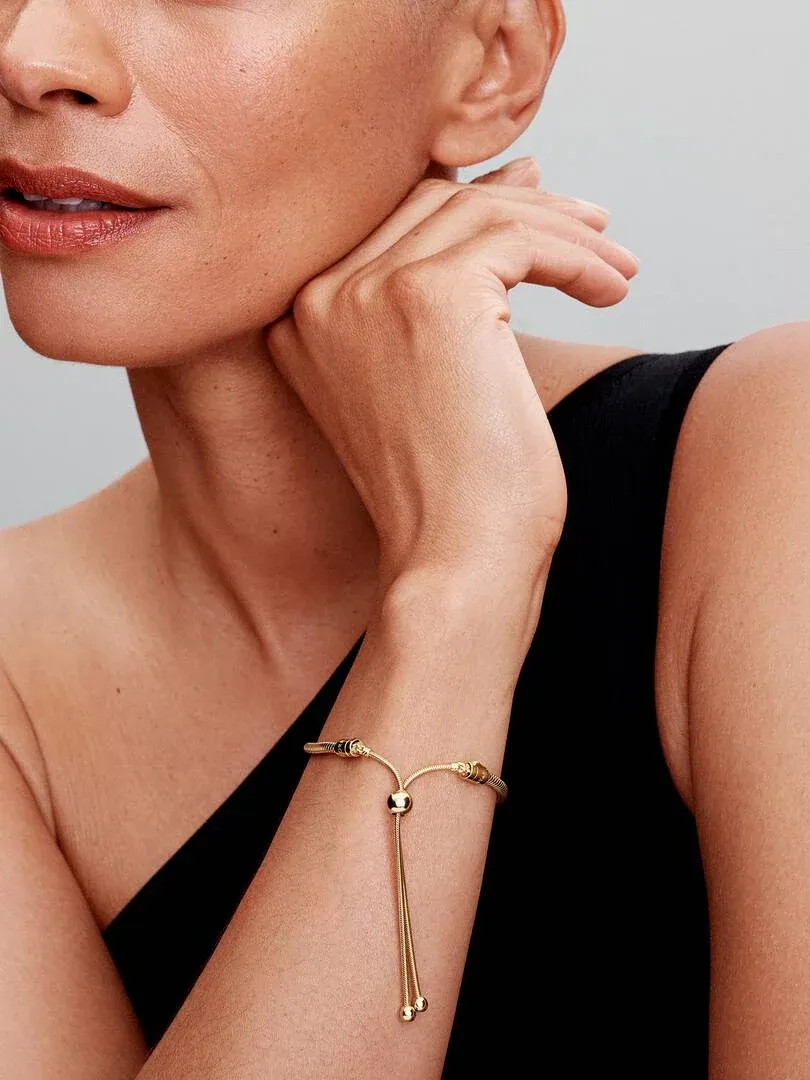 Primer plano de la pulsera dorada con cierre deslizante en la muñeca, toma lateral sobre fondo neutro.