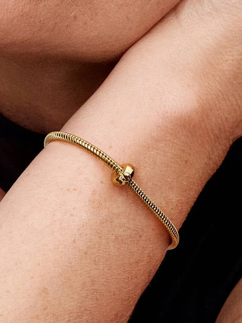 Close-up van gouden armband met clip charm om de pols, zijaanzicht tegen een donkere achtergrond.