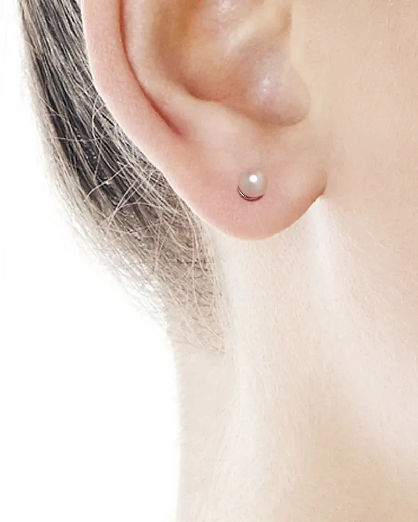 Close-up of pink pearl stud worn on the earlobe, side view against a white background.